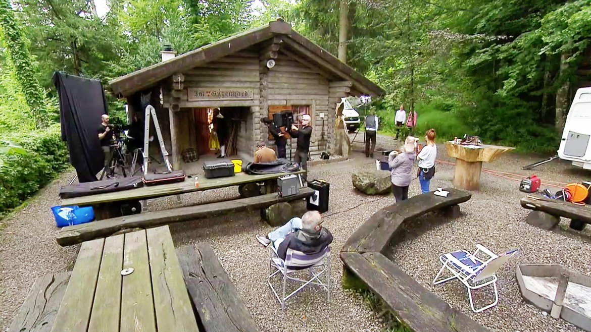 Eine Hütte am Waldrand, um welche verschiedenes Kameraequipment aufgebaut ist