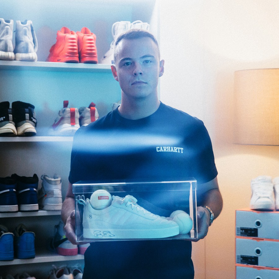 Aron Cash hält ein paar weisse Sneaker in einer Box aus Plexiglas in den Händen
