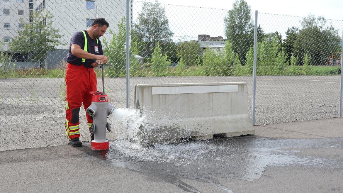 Ein Feuerwehrmann hat einen Hydranten geöffnet, aus welchem Wasser spritzt.