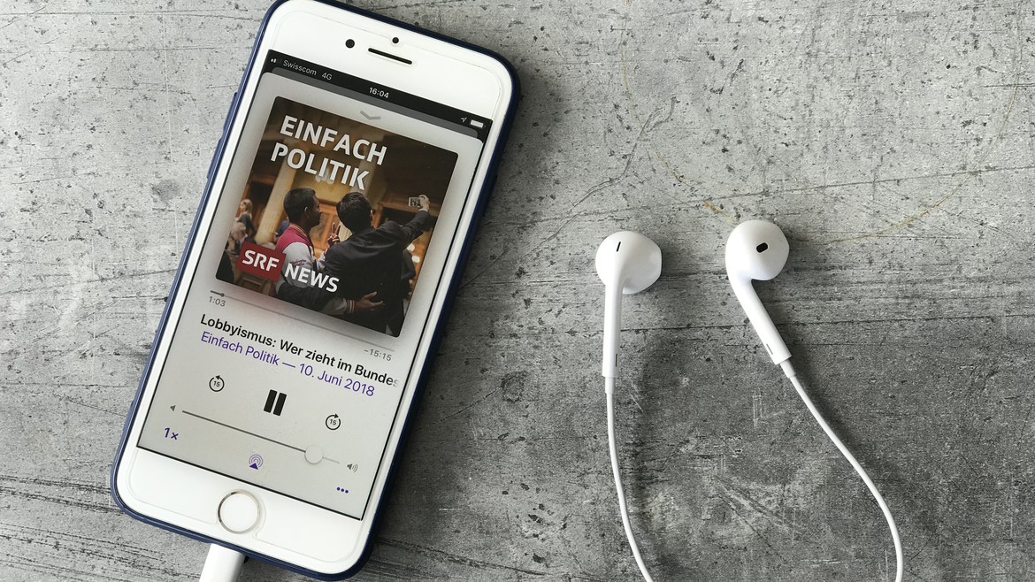 Mobiltelefon mit Podcast-App auf der «Einfach Politik» läuft, daneben Kopfhörer