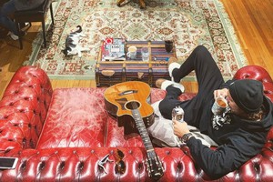 Bastian Baker sitzt im Wohnzimmer auf dem Sofa, neben ihm liegt eine Gitarre