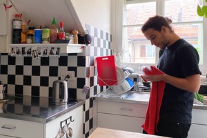 Jan steht zuhause in seiner Küche und trocknet ein Cocktailglas ab