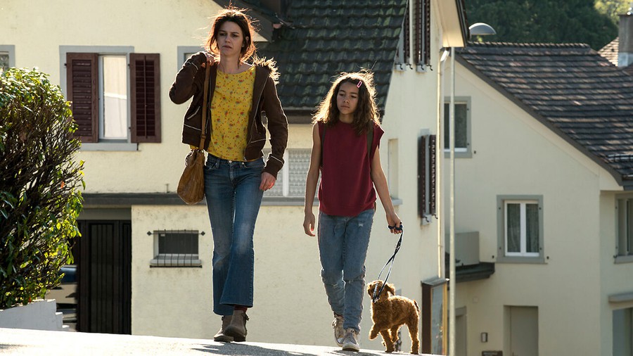 Mia und ihre Mutter laufen mit dem angeleinten Hund eine Strasse im Dorf entlang