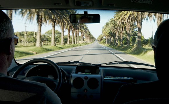 Zwei Männer fahren mit dem Auto durch eine Palmenallee in Uruguay.