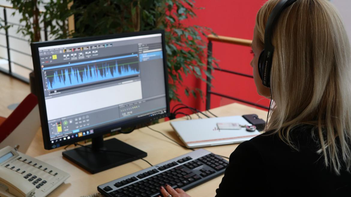 Isabelle Maissen sitzt mit Kopfhörern am Arbeitsplatz und schneidet den Podcast