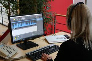 Isabelle Maissen sitzt mit Kopfhörern am Arbeitsplatz und schneidet den Podcast