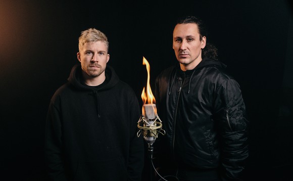 Die beiden Gastgeber Pablo Vögtli und Mauro Wolf stehen vor einem brennenden Mikrofon