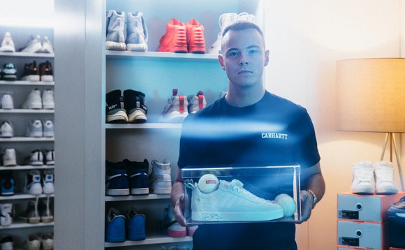Aron Cash hält ein Paar Sneaker in einer Plexiglas-Box in seinen Händen