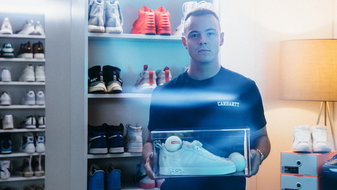 Aron Cash hält ein Paar Sneaker in einer Plexiglas-Box in seinen Händen