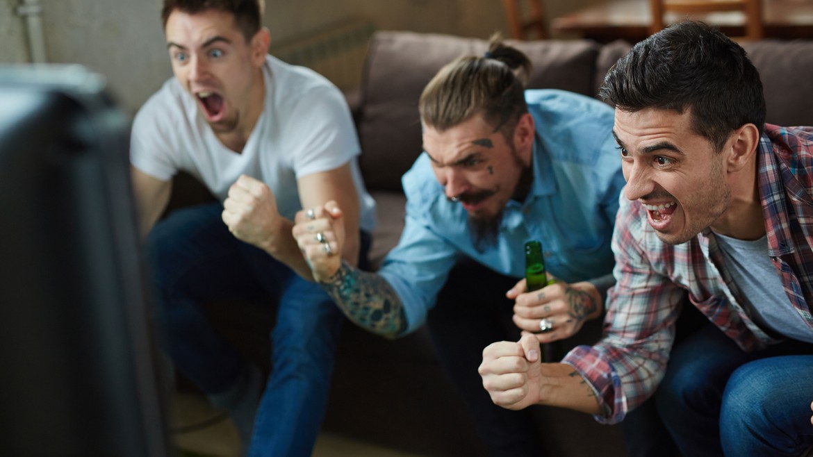 Junge Männer mit Bier jubeln vor dem TV.