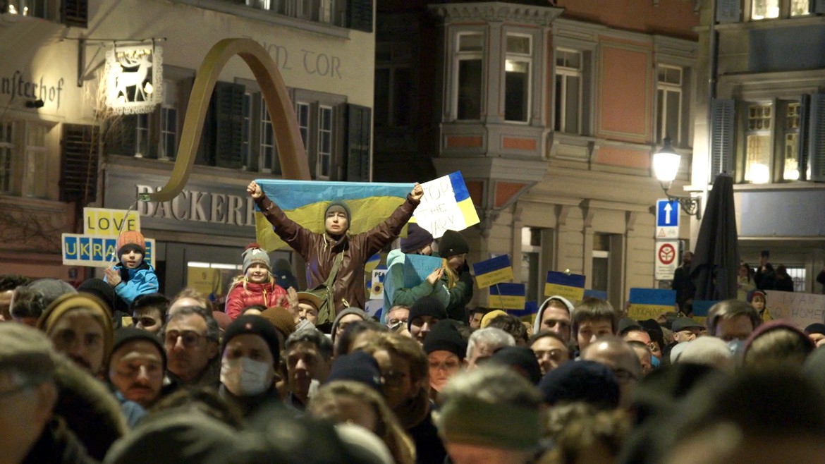 Bild einer Demonstration an der eine Ukraine- Flagge geschwenkt wird.