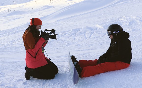 Giulia sitzt mit einem Snowboard an den Füssen im Schnee und wird dabei von Larissa gefilmt