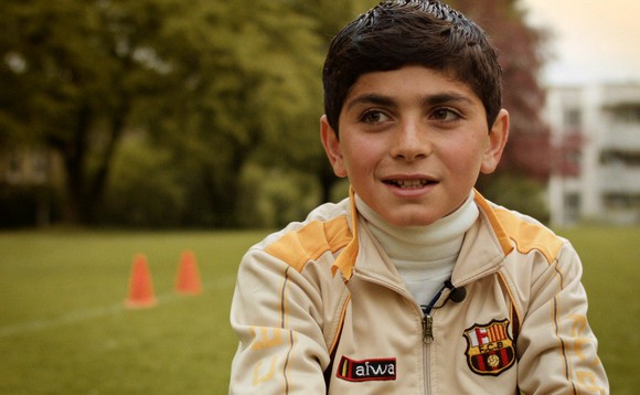 Filmbild zu  «Ayham – Mein neues Leben»: Ein junger Mann sitzt auf dem Rasen.