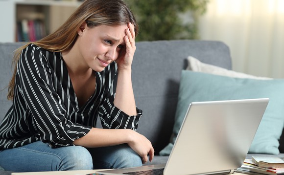 Eine junge Frau schaut zuhause ziemlich verzweifelt auf ihren Laptop-Bildschirm