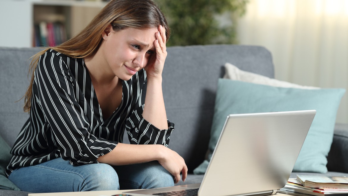 Eine junge Frau schaut zuhause ziemlich verzweifelt auf ihren Laptop-Bildschirm