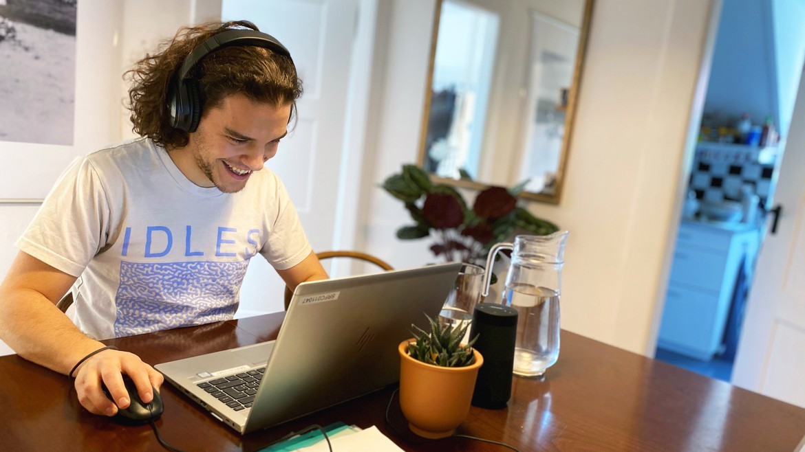 Jan sitzt in seiner Wohnung am Tisch mit Computer und Unterlagen.