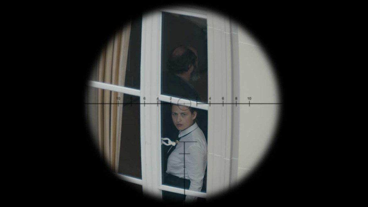 Durch den Sucher einer Waffe ist eine Frau zu sehen, die am Fenster steht