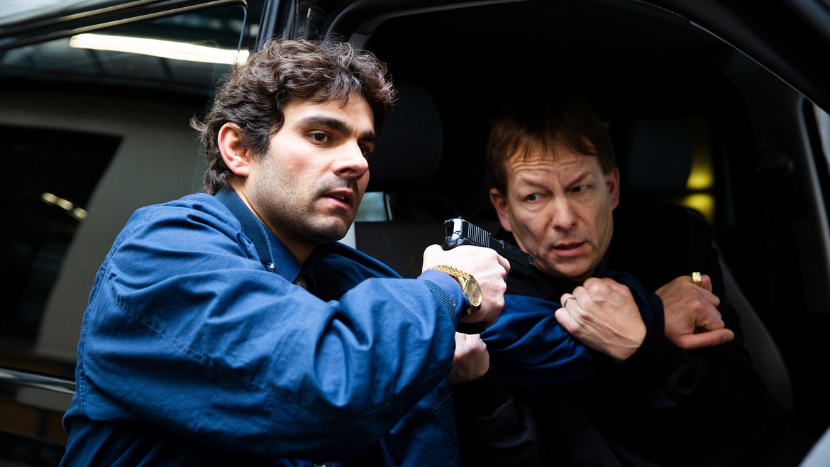 Der Kopf der Bande, Elias A (gespielt von Ivan Georgiev), bedroht den Fahrer des Geldtransport.