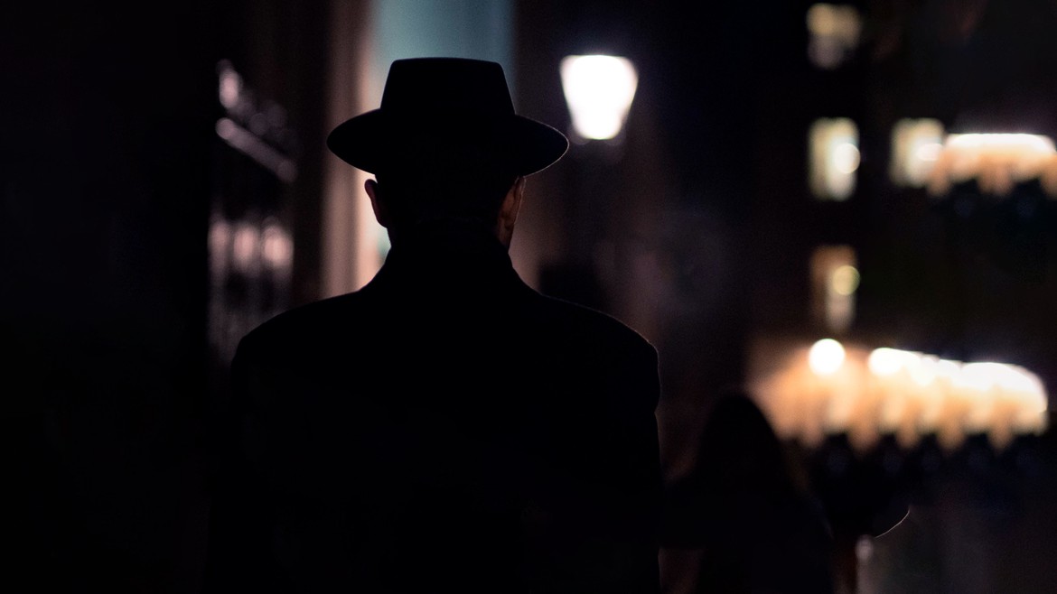 Ein Mann mit Hut läuft durch eine dunkle Strasse