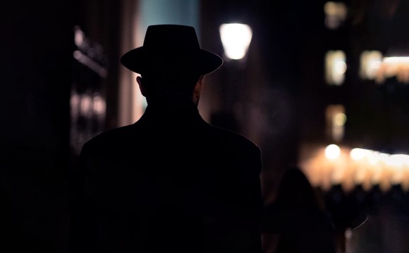 Ein Mann mit Hut läuft durch eine dunkle Strasse