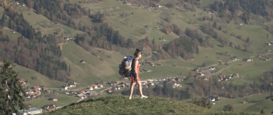 Eine junge Frau mit einem grossen Rucksack steht auf einem Hügel