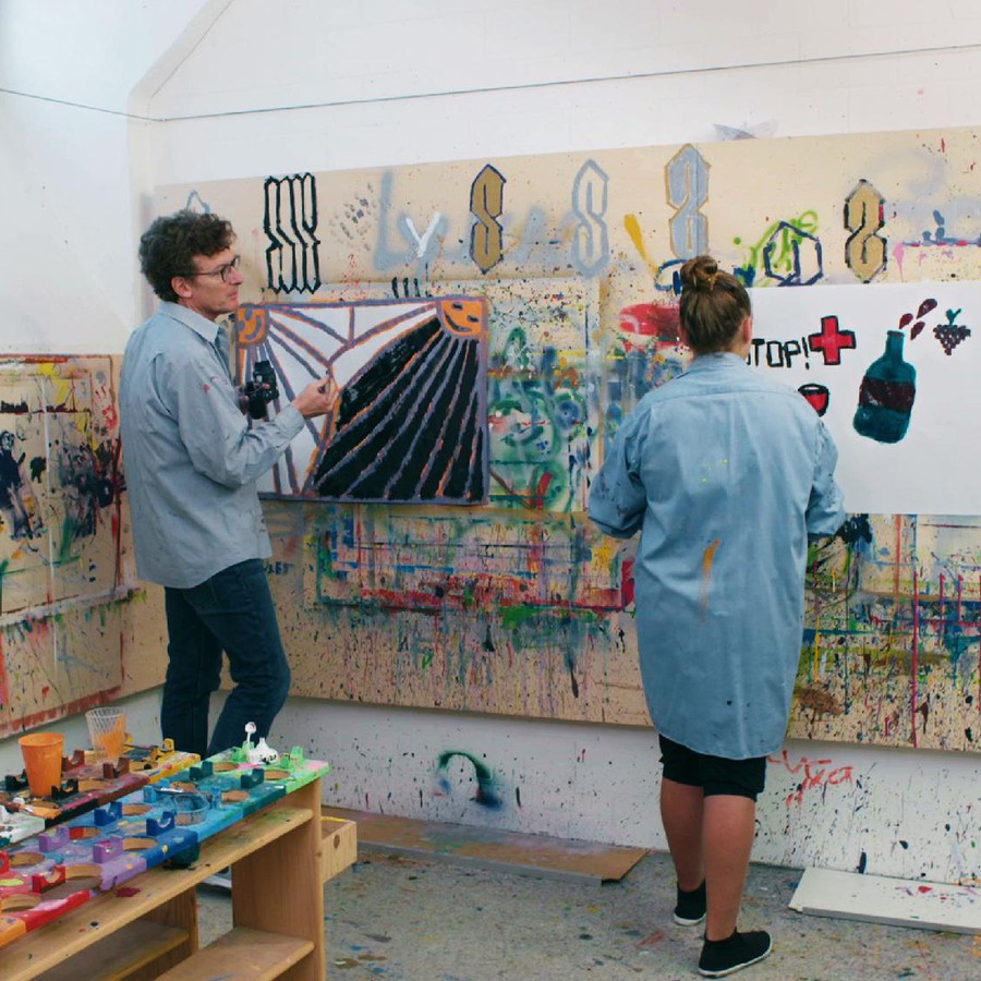 Georg und Zoe stehen mit Pinseln ausgerüstet vor einer farbig bemalten Wand
