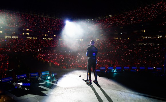 Colplay-Frontmann Chris Martin im Spotlight auf der Bühne. Vor ihm ist das Publikum zu sehen.