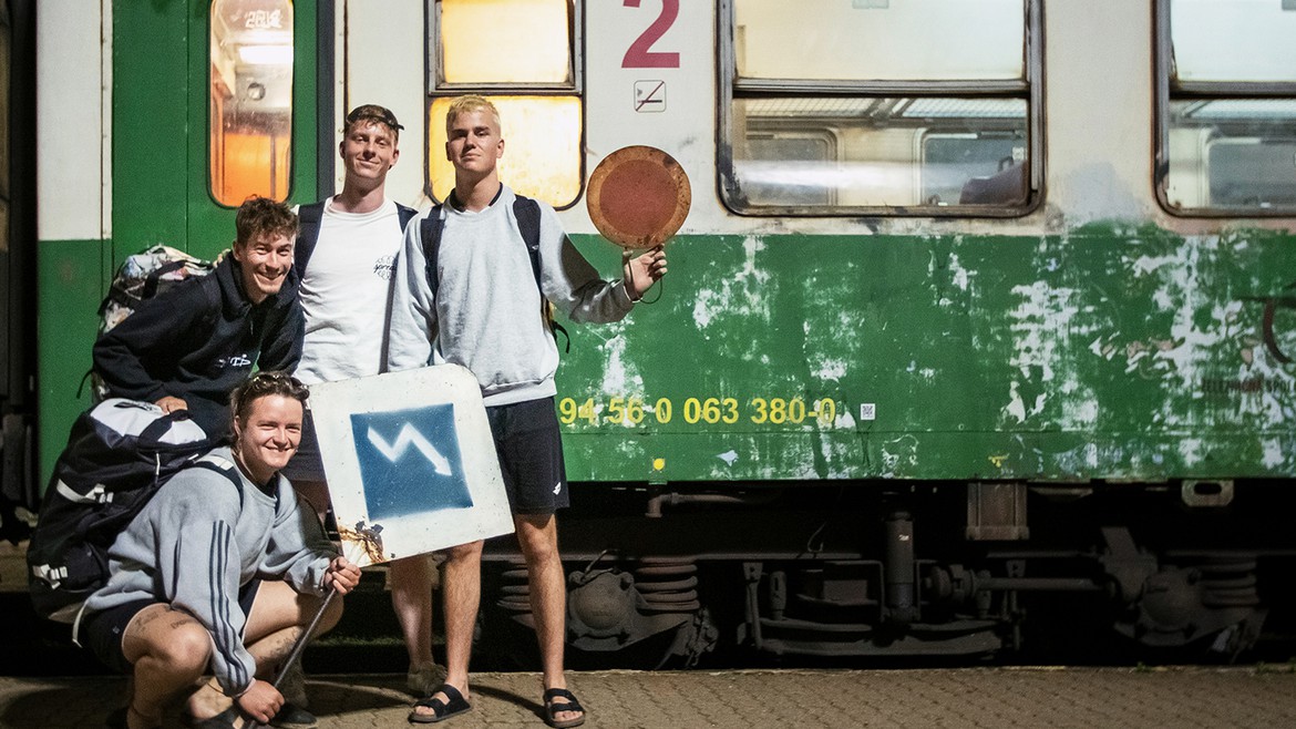 Vier Jungs posieren mit ihren Rucksäcken vor einem grünen Zug im Osten der Slovakei.